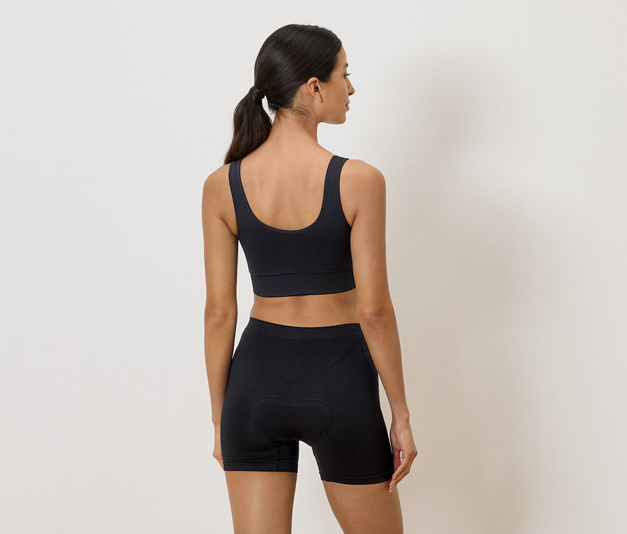 Nötr bir arka planda siyah sporcu sütyeni ve şortlu bir kadın arkadan.