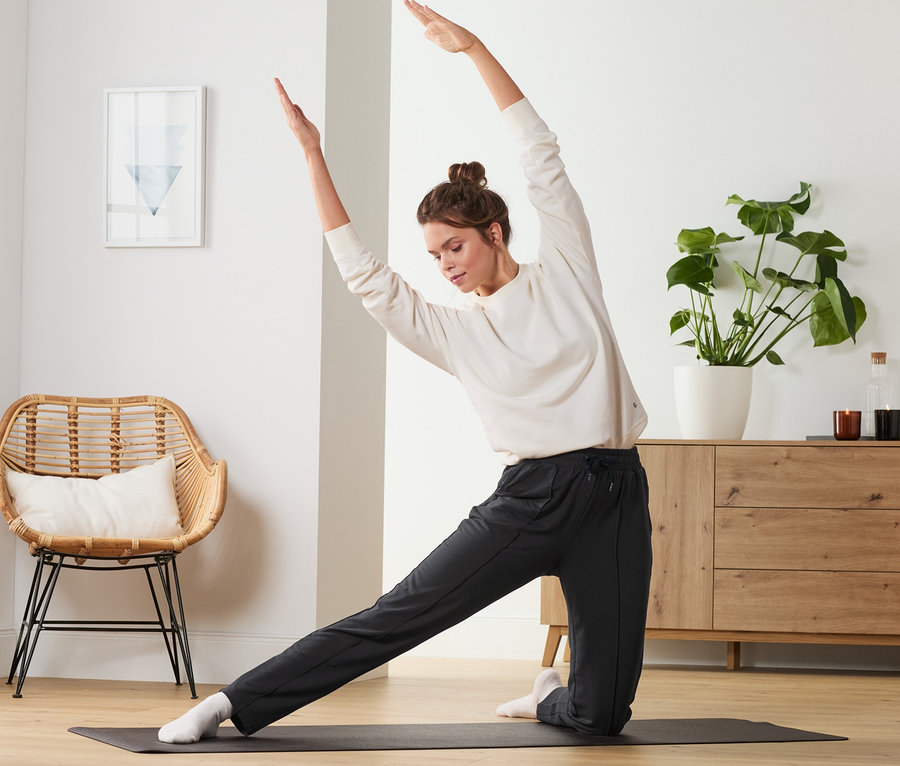 Kadın yoga matında egzersiz yapıyor ve siyah eşofman altı giyiyor.