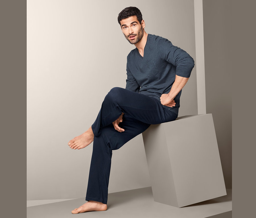 Adam gri bir küpün üzerinde oturuyor ve üzerinde Organik Pamuklu Pijama Takımı var.