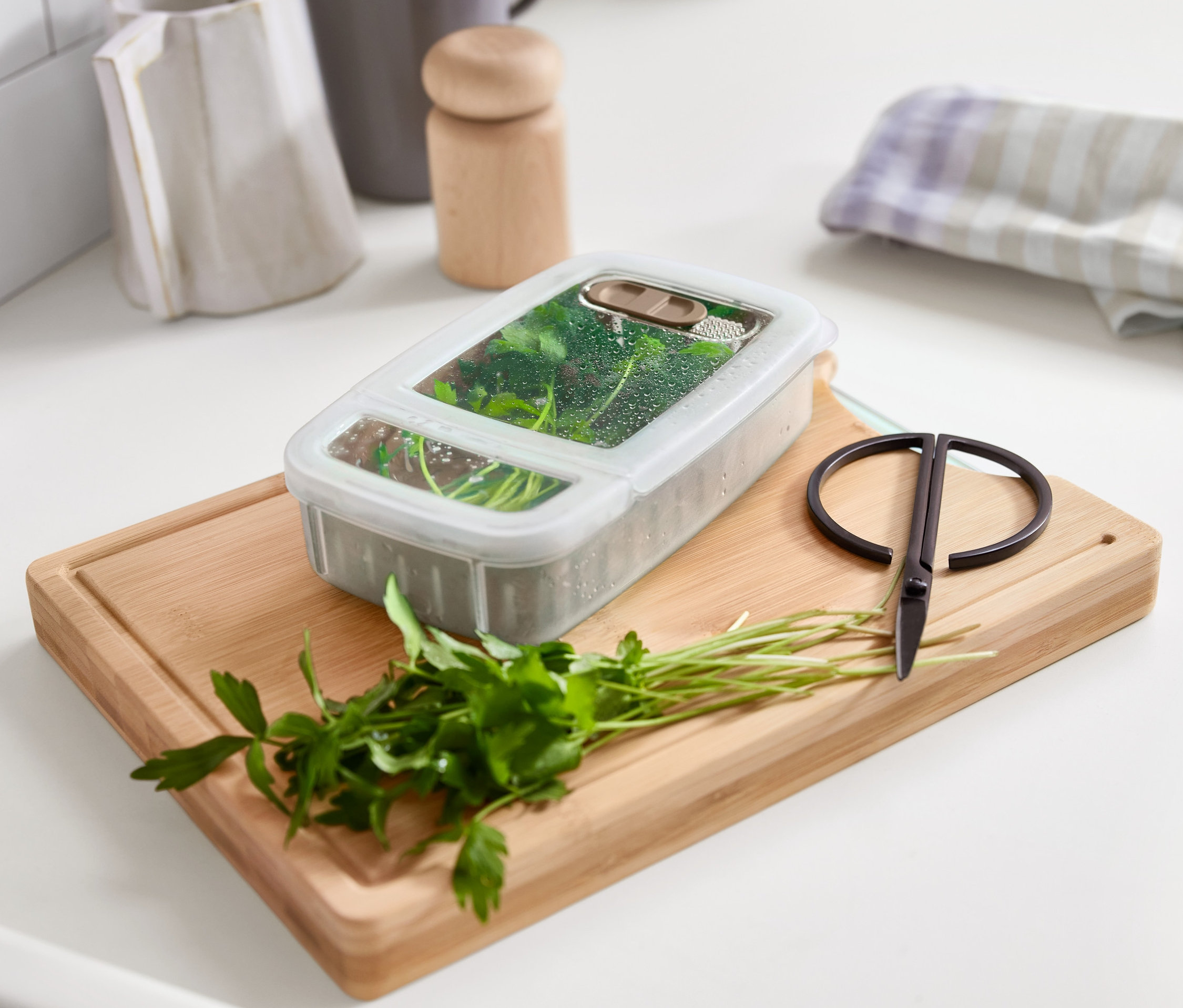 Yeşillik saklama kabı, maydanoz ve makasla birlikte bir tahta üzerinde duruyor.