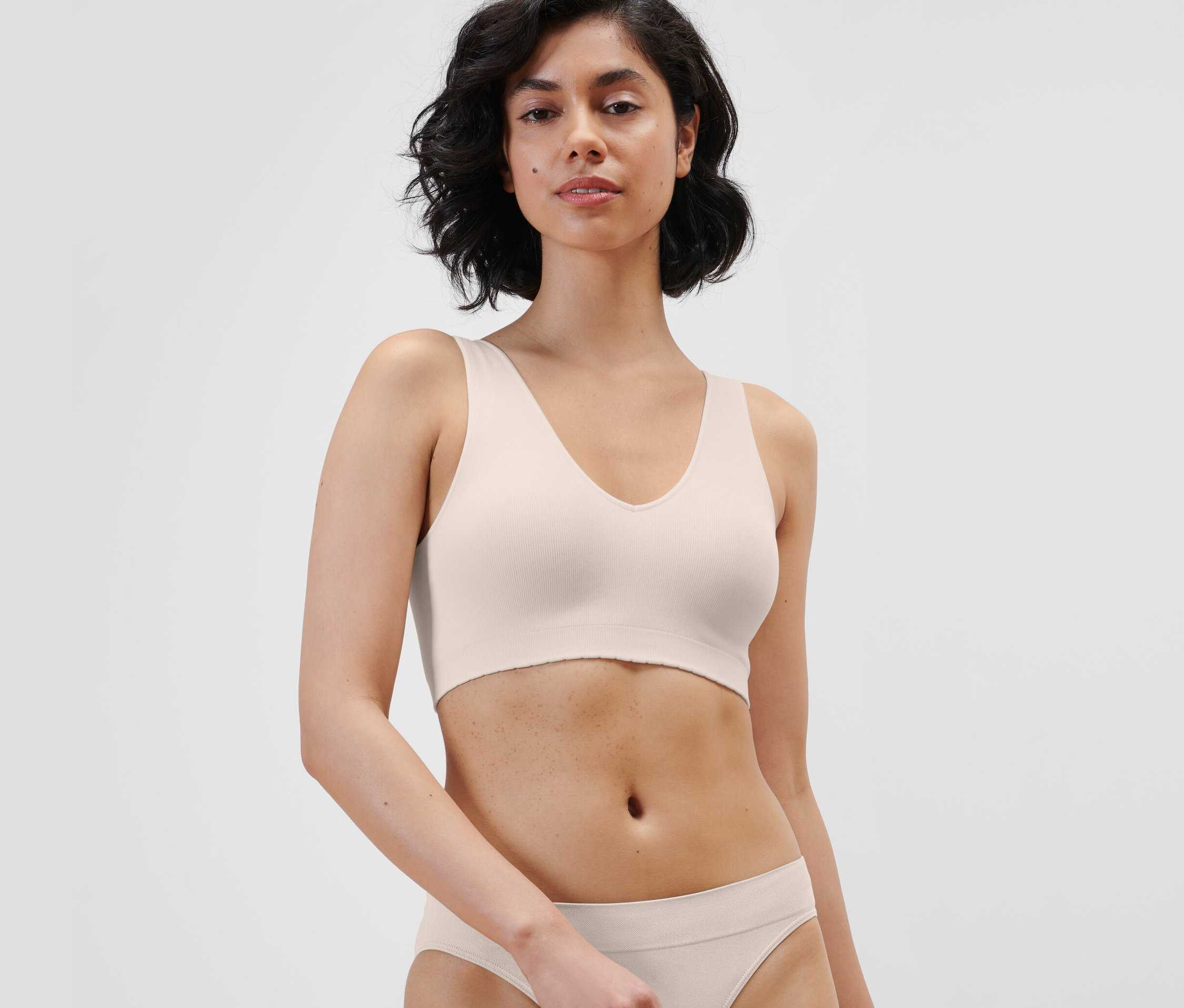 Kadın krem rengi dikişsiz bir büstiyer ve alt giyim giyiyor.