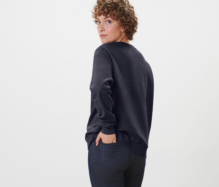 Omuzunun üzerinden bakan kadın lacivert organik pamuklu sweatshirt ile poz veriyor.