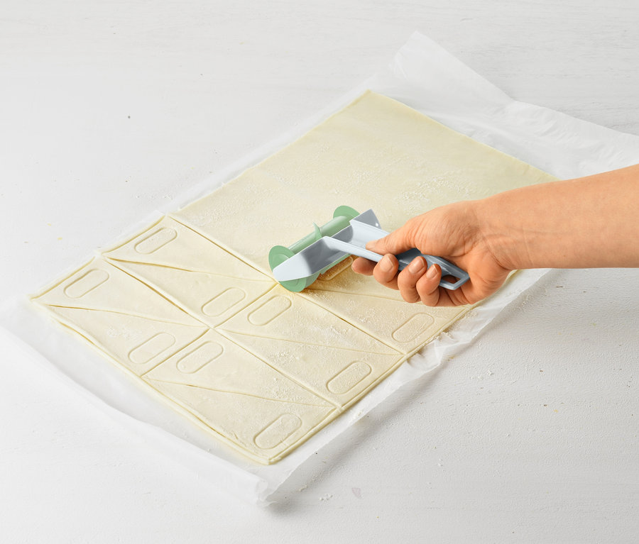 Bir el, hamuru üçgenler halinde kesmek için bir kruvasan rulosu kullanıyor.