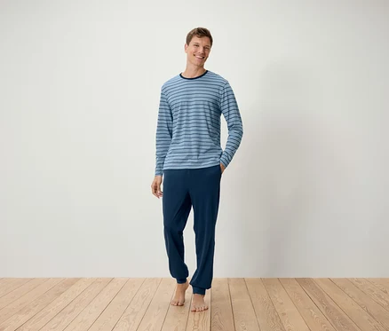 Adam yerde çıplak ayakla duruyor, açık mavi çizgili bilek bantlı pijama takımı giyiyor.