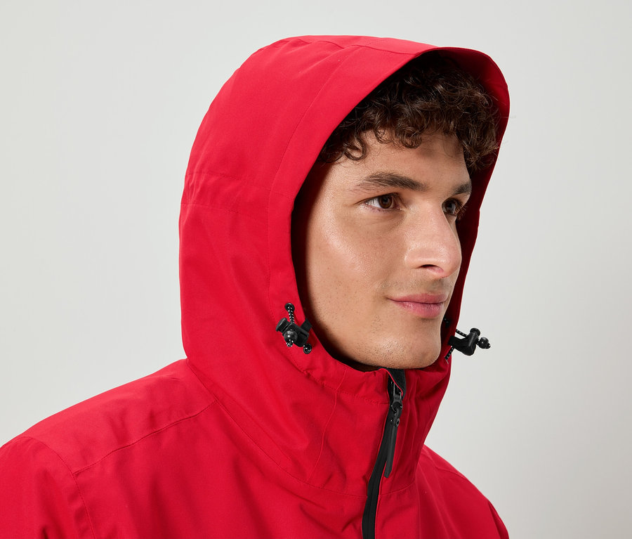 Kıvırcık saçlı bir adam kırmızı kapüşonlu bir ceket giyiyor.