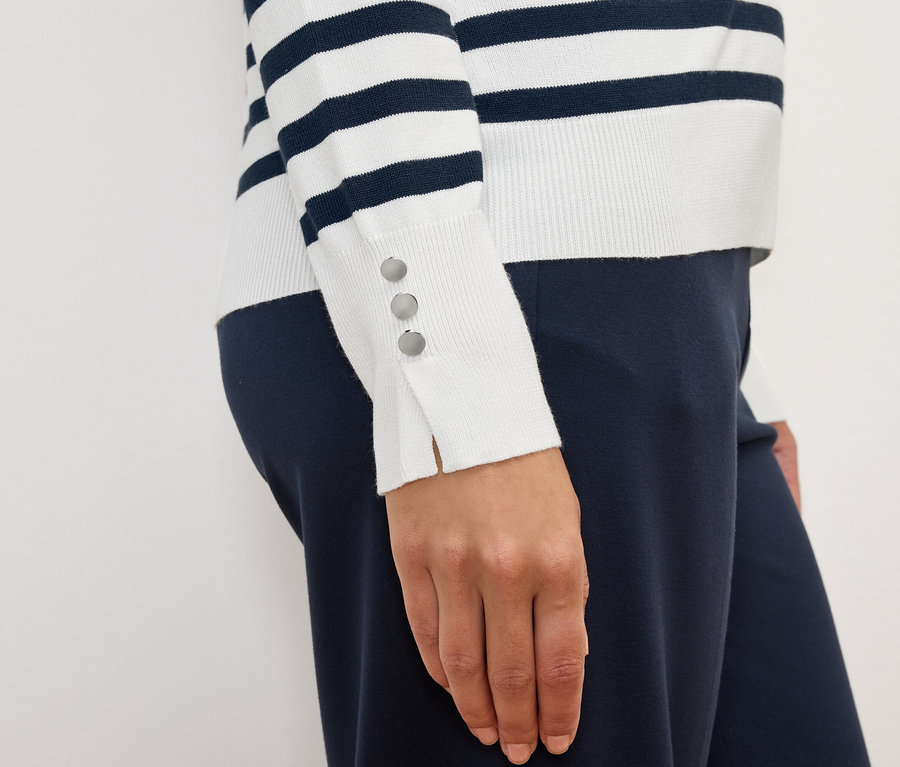 Kadın, manşetlerinde düğmeleri olan çizgili, uzun kollu bir kazak ve lacivert pantolon giyiyor.