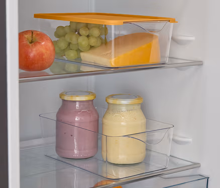 Elma, üzüm, peynir, iki smoothie bardağı, bir portakal ve misket limonları ile dolu açık bir buzdolabı.
