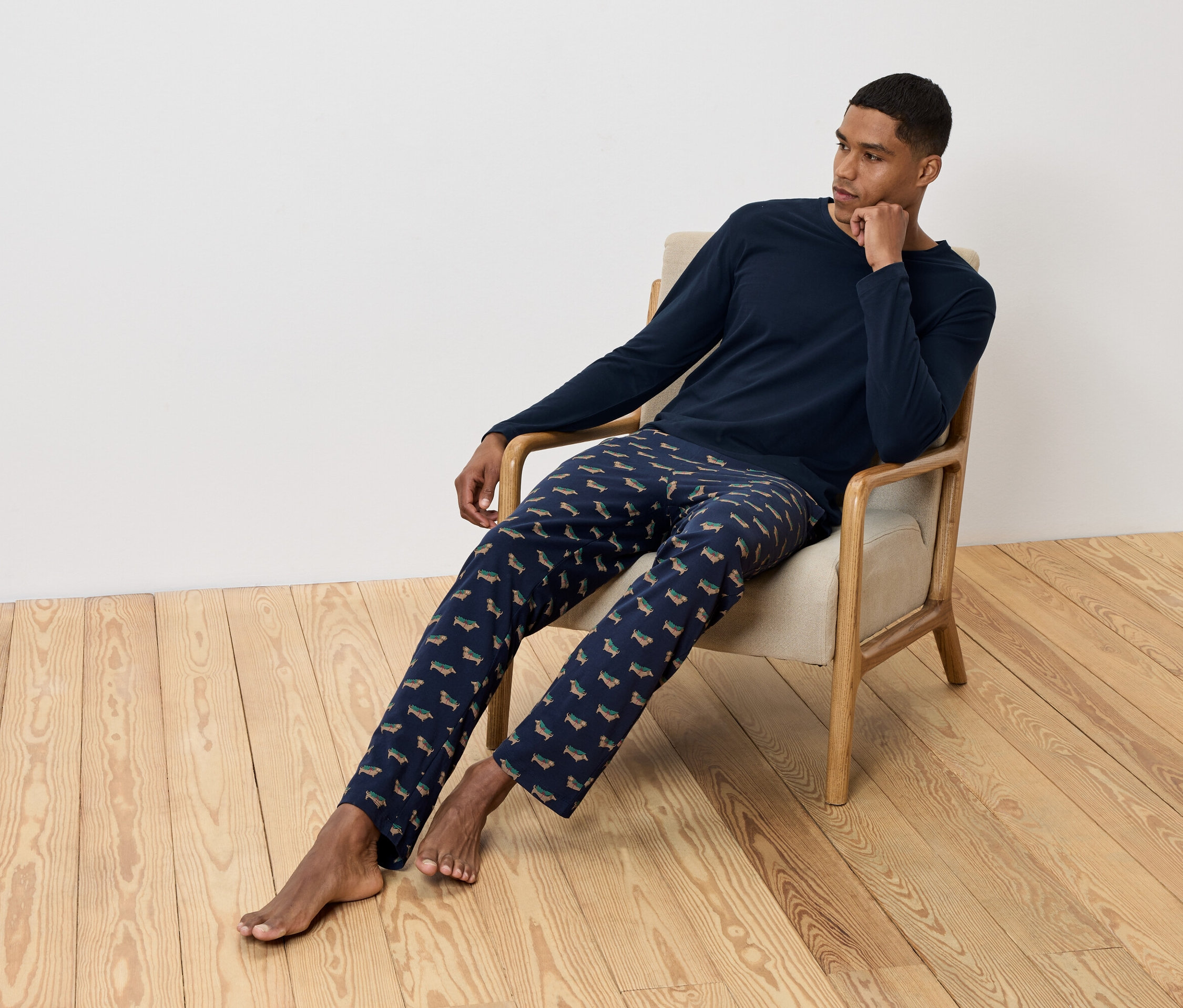 Bir adam koltukta oturuyor ve üzerinde dachshund baskılı lacivert bir pijama var.