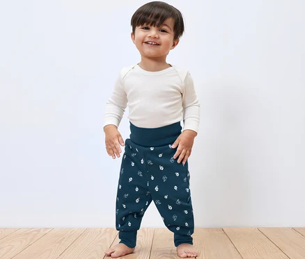 Gülümseyen küçük bir erkek çocuk stüdyoda poz veriyor ve üzerinde 2 Adet Bebek Sweat Pantolon var.