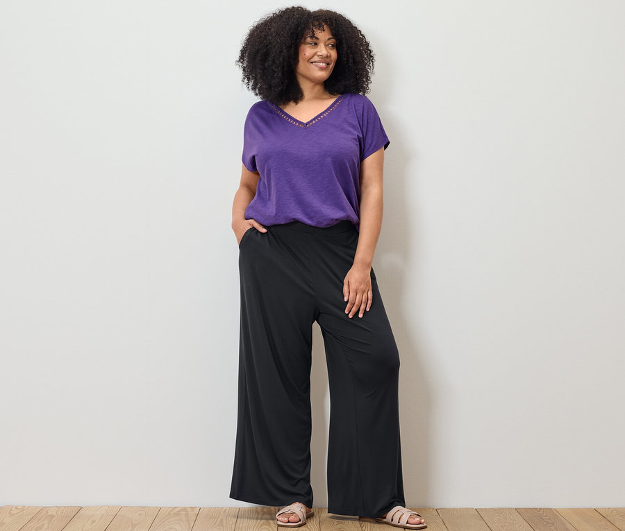 Kadın mor modal karışımlı tişört ve siyah palazzo pantolonla poz veriyor.