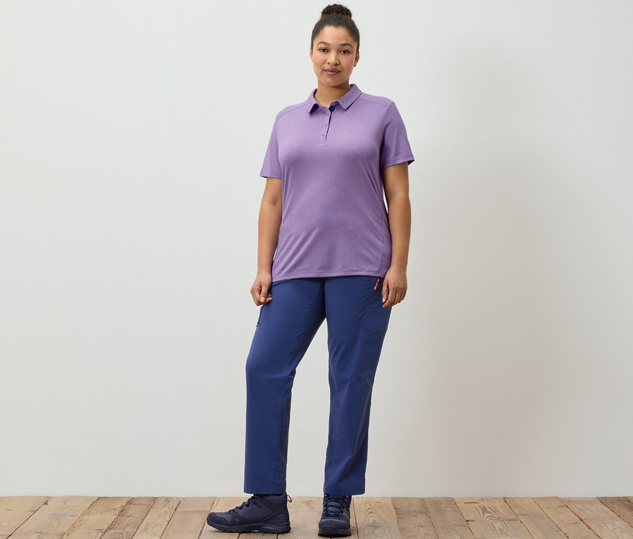 Bir kadın, lacivert, kendi cebine toplanabilir outdoor pantolonu ve mor fonksiyonel polo tişörtü ile ahşap zeminde poz veriyor.