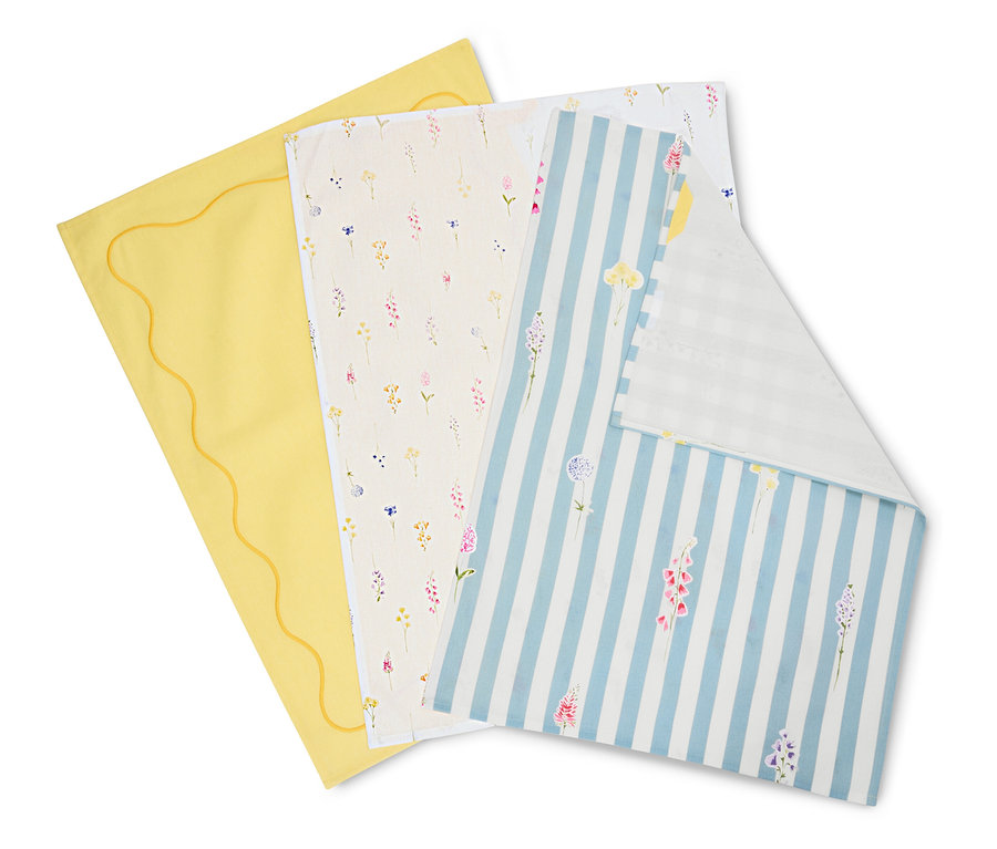 Üç bez üst üste duruyor: biri dalgalı kenarlı sarı, biri çiçek desenli krem rengi ve biri çiçekli mavi-beyaz çizgili.