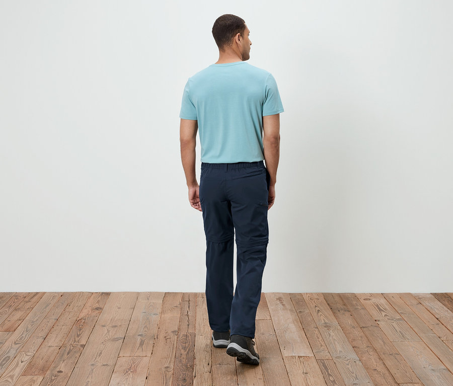 Arkadan görünen bir adam, turkuaz tişört ve lacivert pantolon giymiş, ahşap zeminde yürüyor.