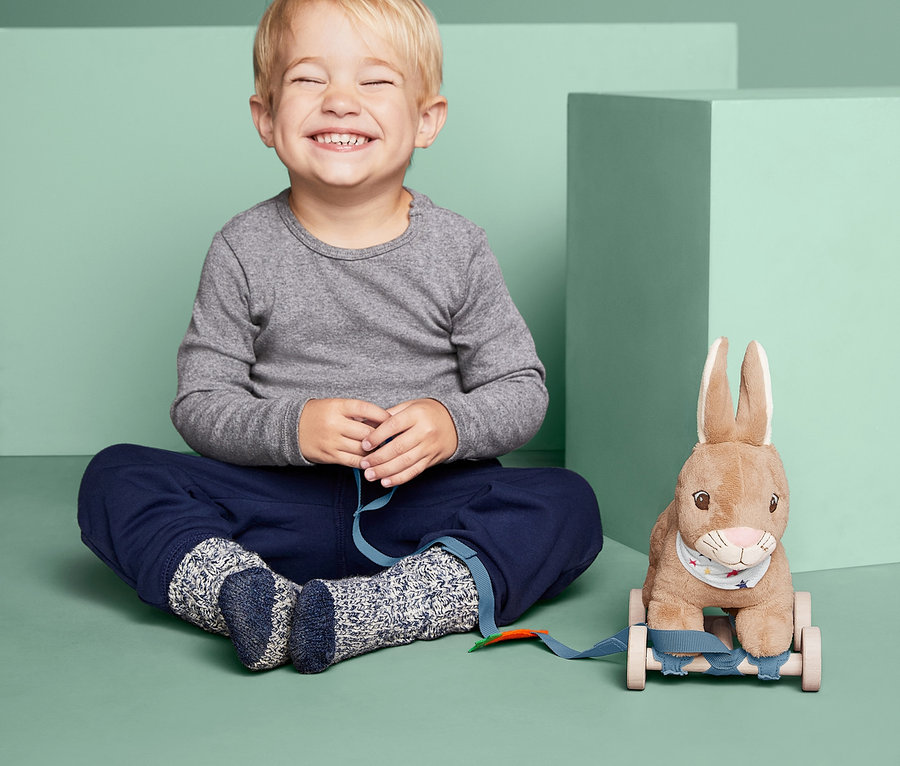 Gözleri kapalı bir erkek çocuk, Tekerlekli Oyuncak »Zıplayan Tavşan« oyuncağının yanında oturuyor.