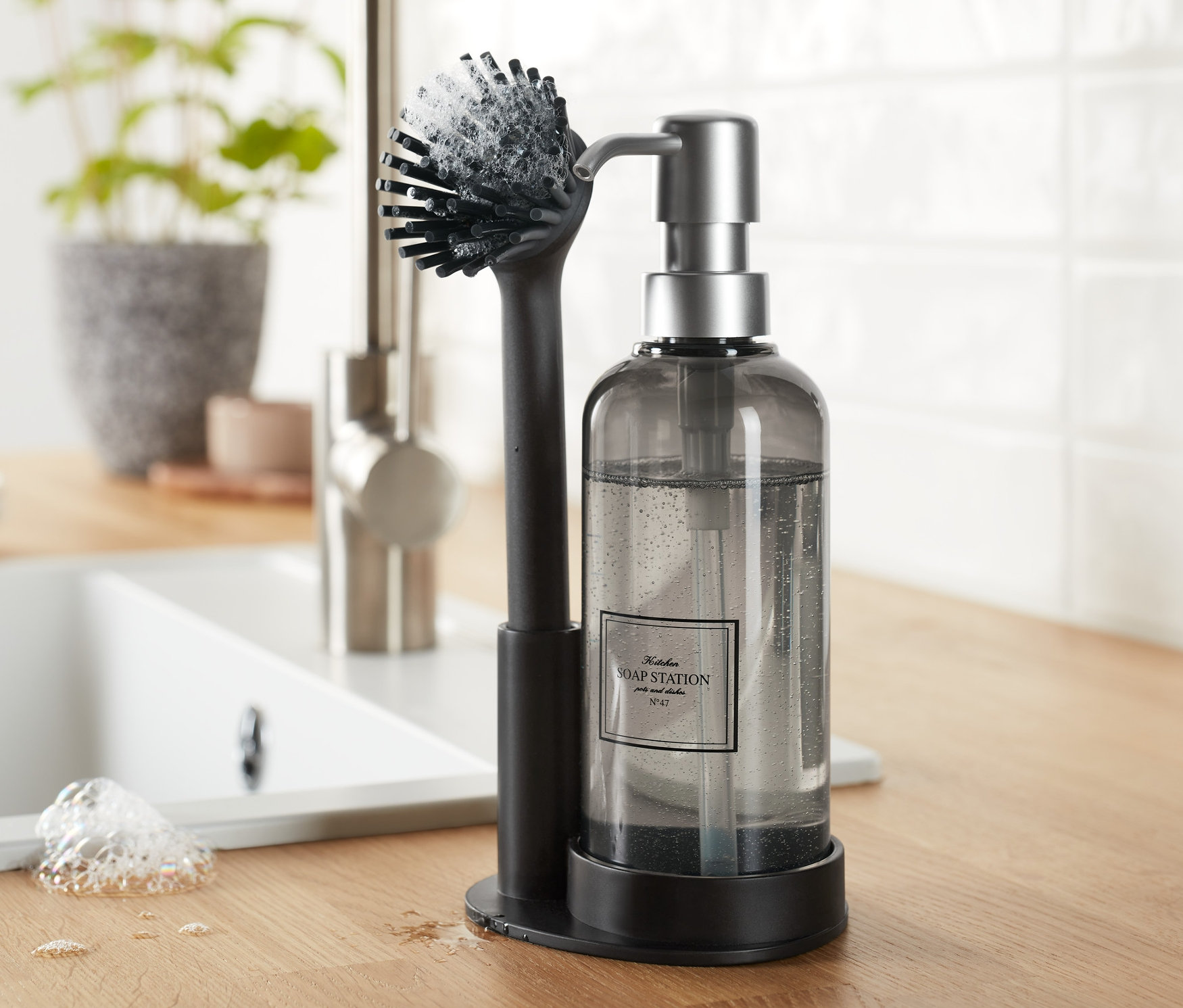 Bulaşık yıkama setinden siyah bulaşık fırçası ve bulaşık deterjanı dispenseri, tezgah üzerinde lavabonun yanında duruyor.