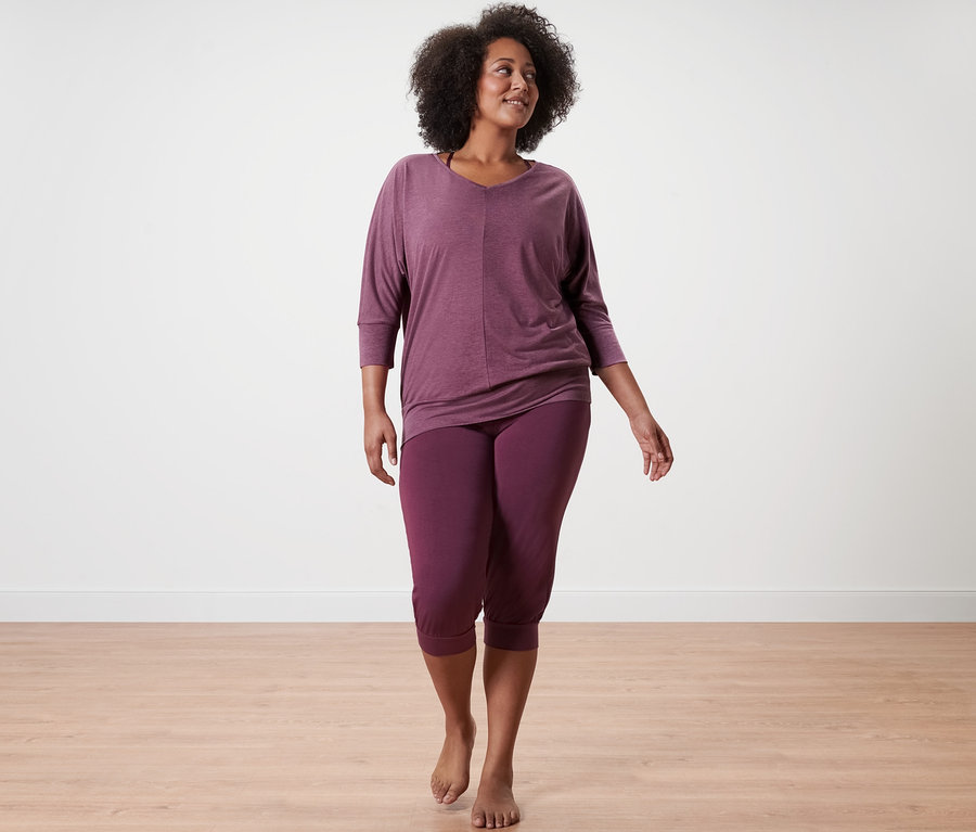 Kadın yürüyor, üzerinde mürdüm rengi 3/4 yoga pantolonu ve mürdüm rengi yoga üstü var.