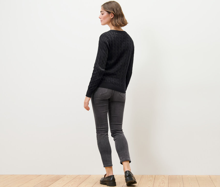 Kadın Saç Örgüsü Motifli İnce Örgü Hırka, kot pantolon ve mokasen giyiyor.