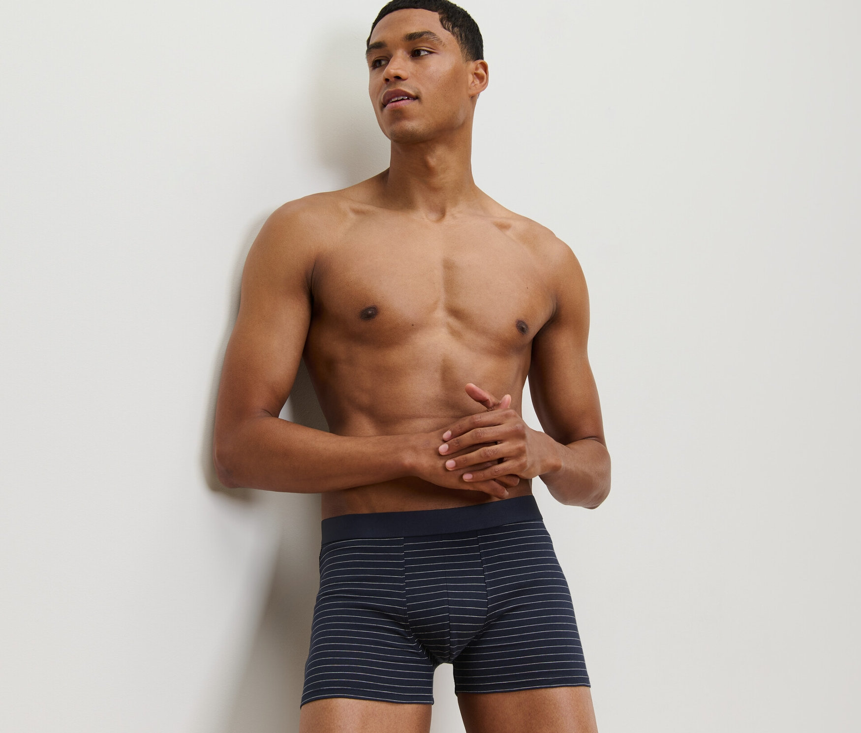 Duvara yaslanmış bir adam, 2'li Slip Boxer setinden birini giyiyor.