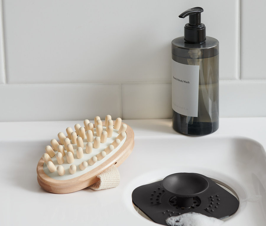 Lavaboda bir gider süzgeci/tıpa, yanında bir masaj fırçası ve bir sabun şişesi bulunmaktadır.