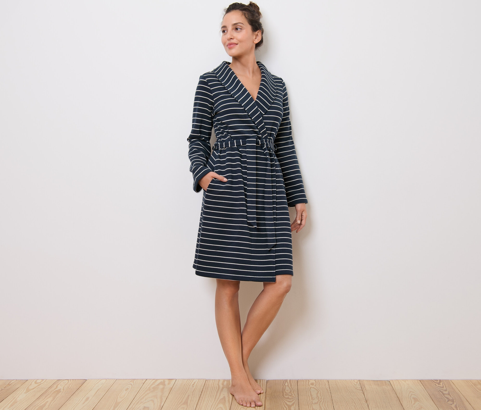 Kadın ayakta duruyor, çizgili sabahlık giyiyor.