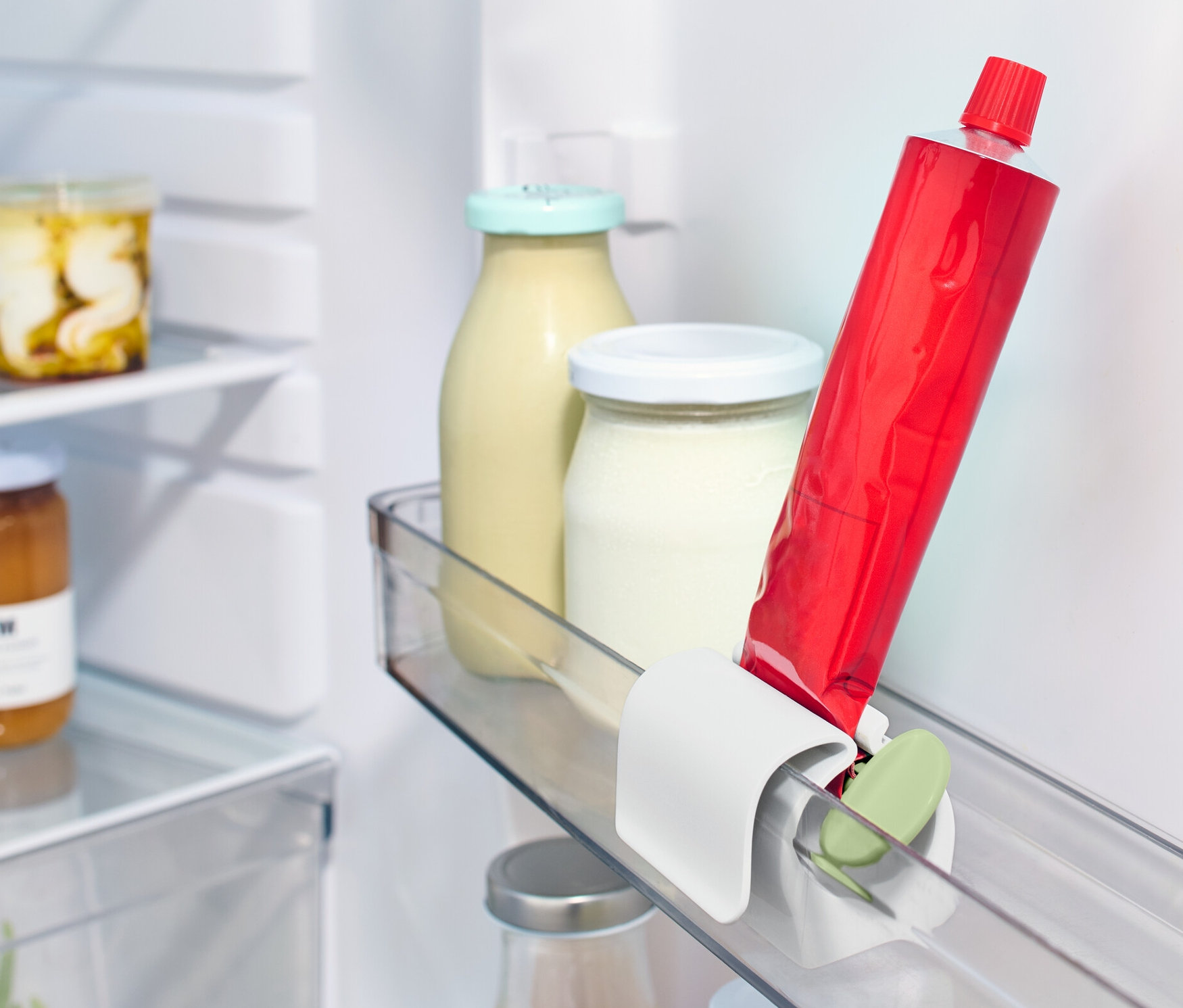 Kırmızı bir tüp, diğer yiyeceklerin yanında buzdolabı rafında bir Buzdolabı Klipsli Tüp Sıkacağı içinde duruyor.