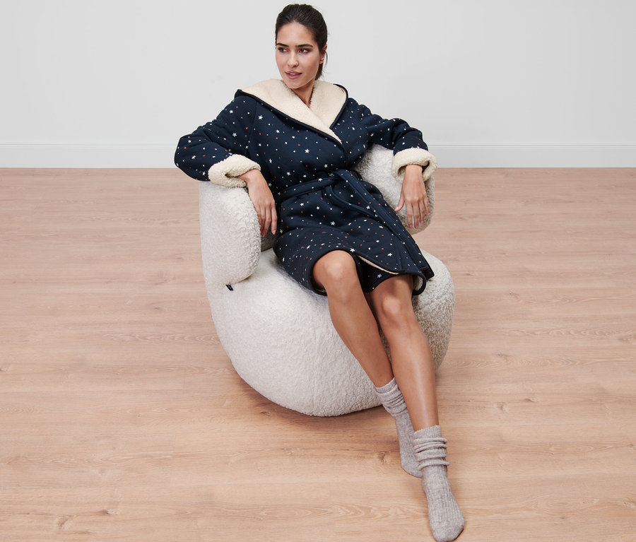 Kadın koltukta oturuyor ve Pelüş Bornoz giyiyor.