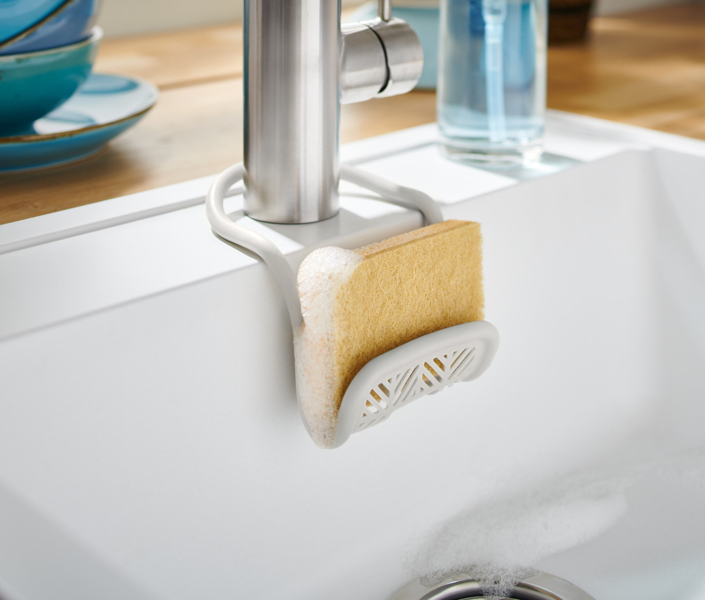 Beyaz bir lavaboda musluğa takılı süngerli süngerlik.