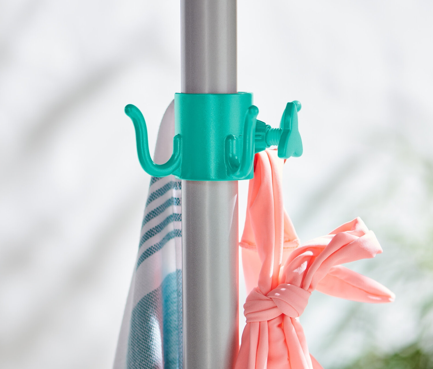 Gümüş bir çubuğa takılmış, üzerinde havlu ve pembe giysiler asılı duran iki adet güneş şemsiyesi askısı.