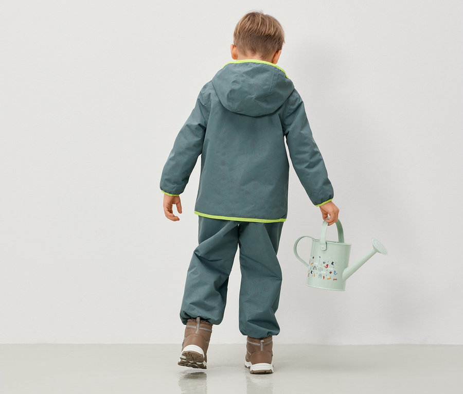 Kapüşonlu ceket ve pantolon giyen çocuk sulama kabı tutuyor.