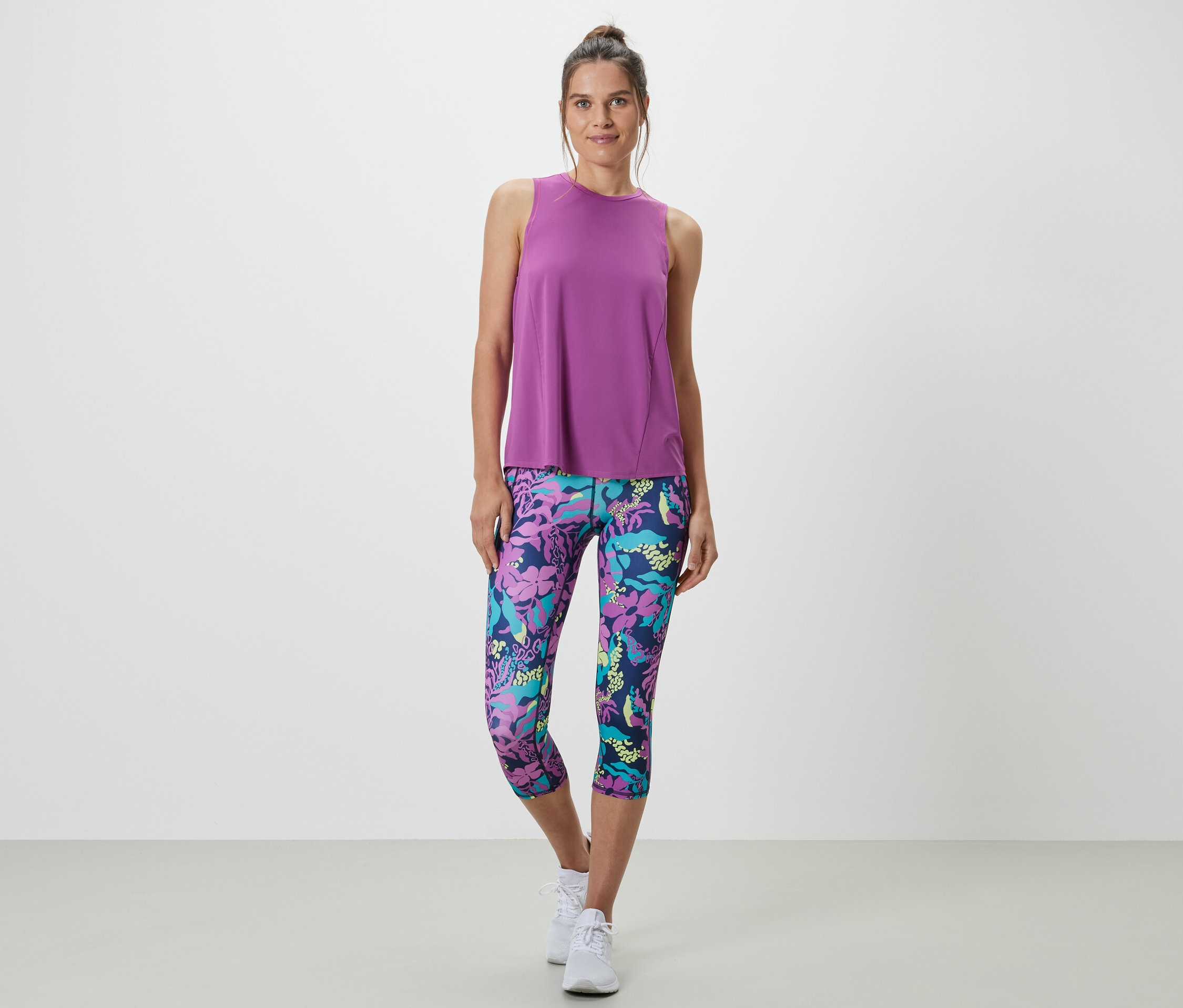 Kadın, iki parçalı bir takımdan turkuaz bir sporcu atleti ve çiçek desenli bir tayt giyiyor.