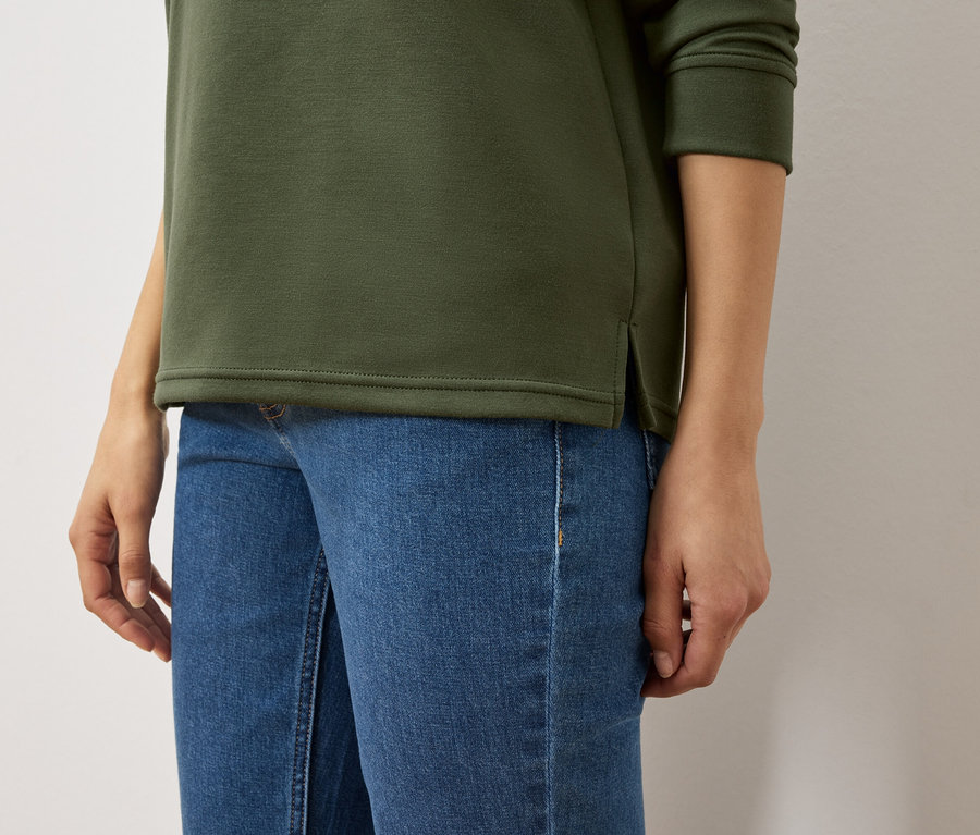 Zeytin yeşili sweatshirt ve mavi kot pantolonlu bir kadının gövdesi