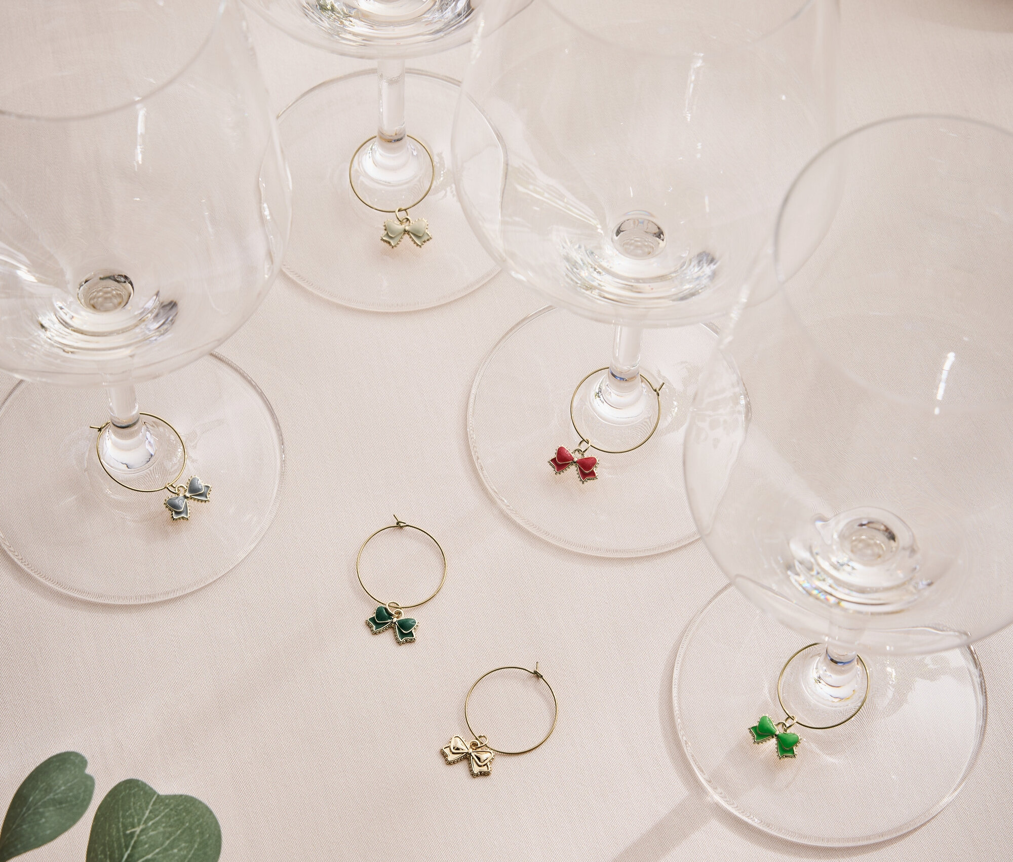 Açık renkli bir yüzeyde bitki yaprağıyla birlikte, saplarında renkli kurdeleler bulunan altı adet boş şarap kadehi.