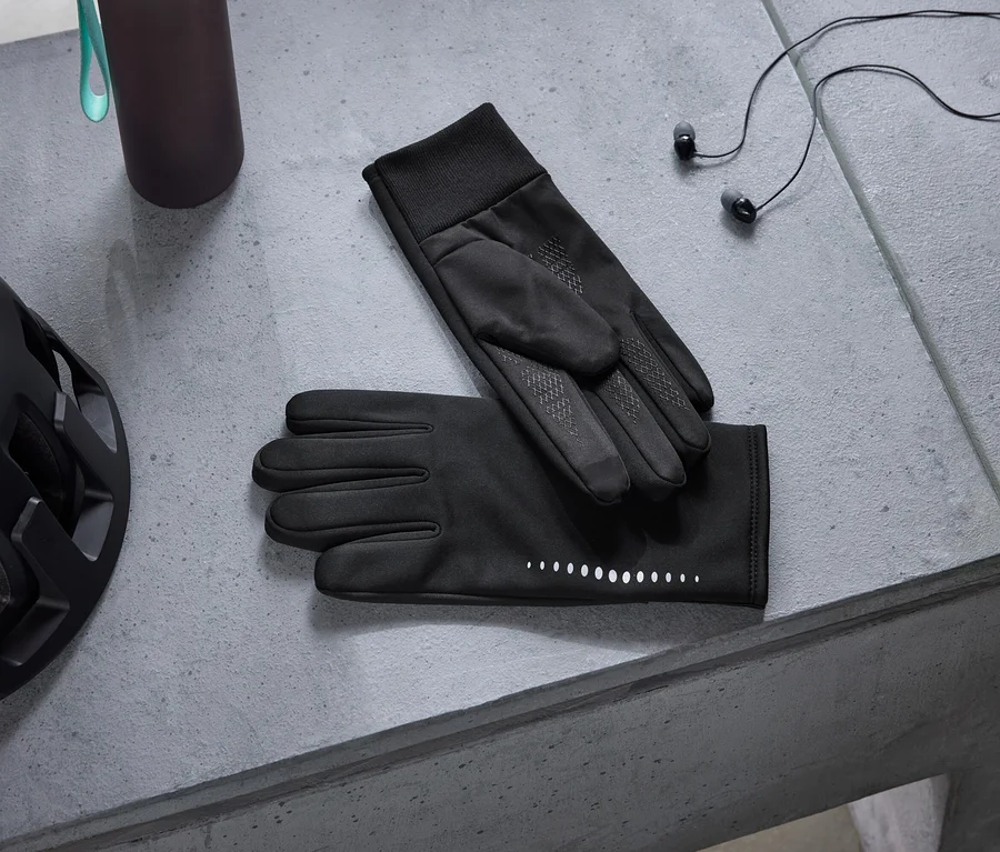 Siyah bisiklet kaskı, koyu renk su şişesi, yansıtıcı noktalı siyah eldivenler ve siyah kulaklıklar gri beton yüzeyde duruyor.