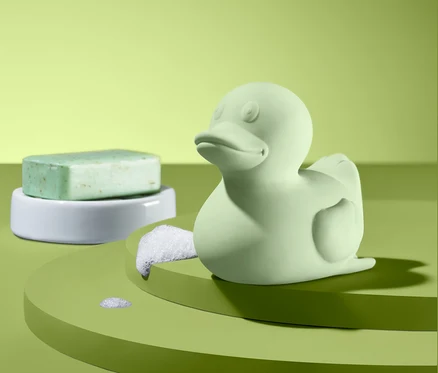 Yeşil renkli küçük bir banyo ördeği ve beyaz bir stand üzerinde yeşil sabun.
