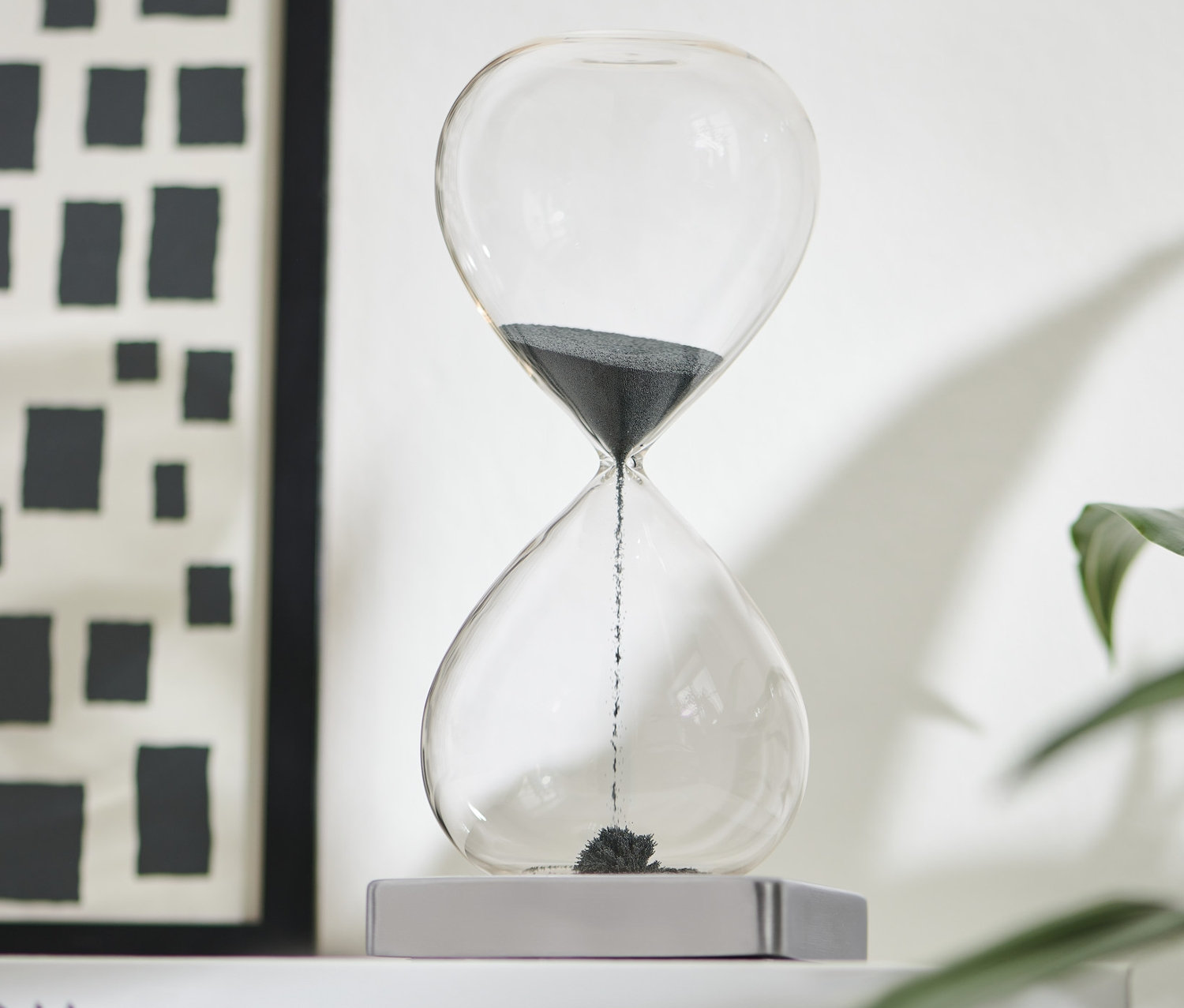 Beyaz bir kitap üzerinde siyah manyetik kum saati. 