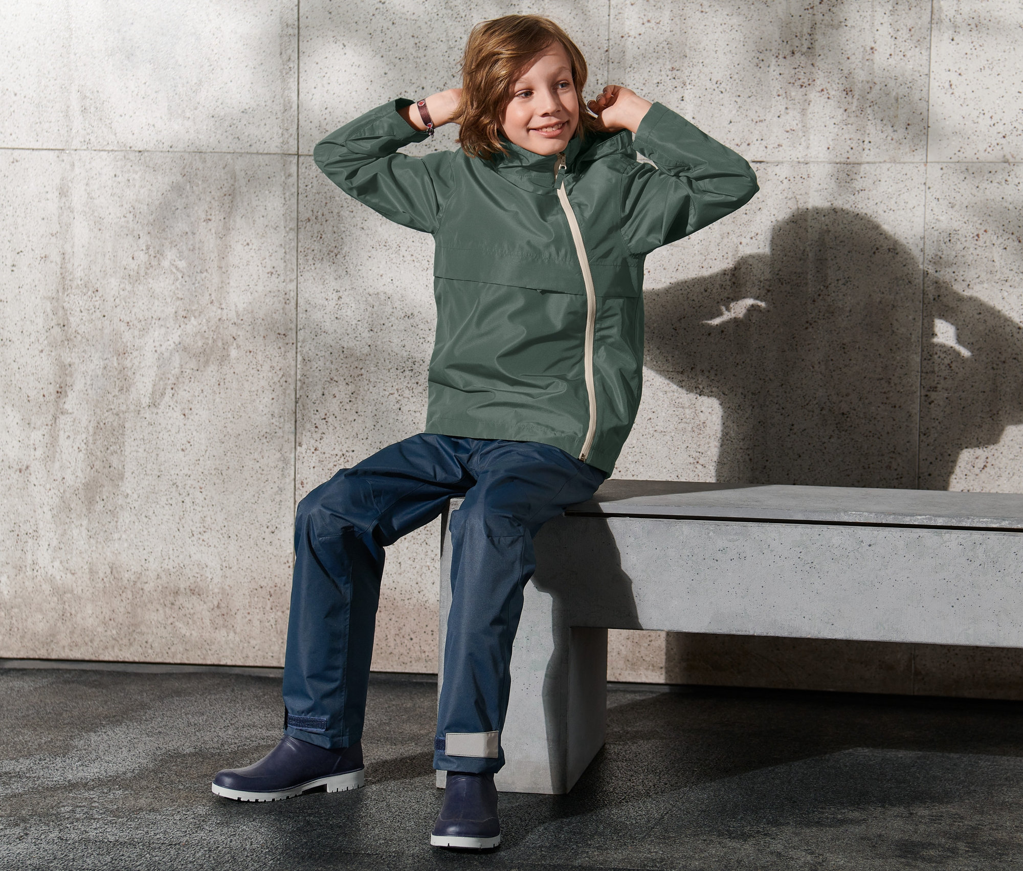 Bankta oturan bir çocuk Mevsimlik Ceketinin kapüşonunu ayarlıyor.