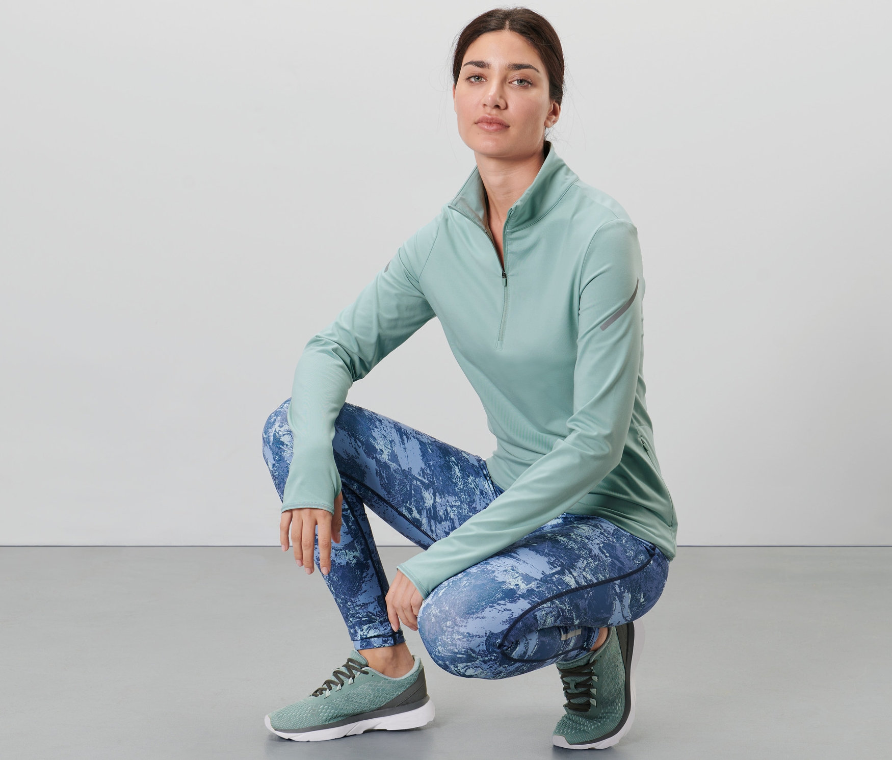 Çömelmiş bir kadın su yeşili fonksiyonel termal üst ve desenli tayt giyiyor.