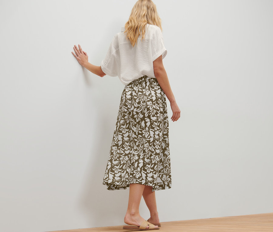 Kadın baskılı midi etek ve beyaz gömlekle poz veriyor.