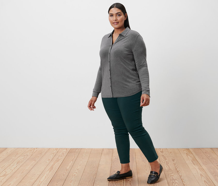 Kadın yürüyor, üzerinde düğmeli kırçıllı gri bluz, streç pantolon var.
