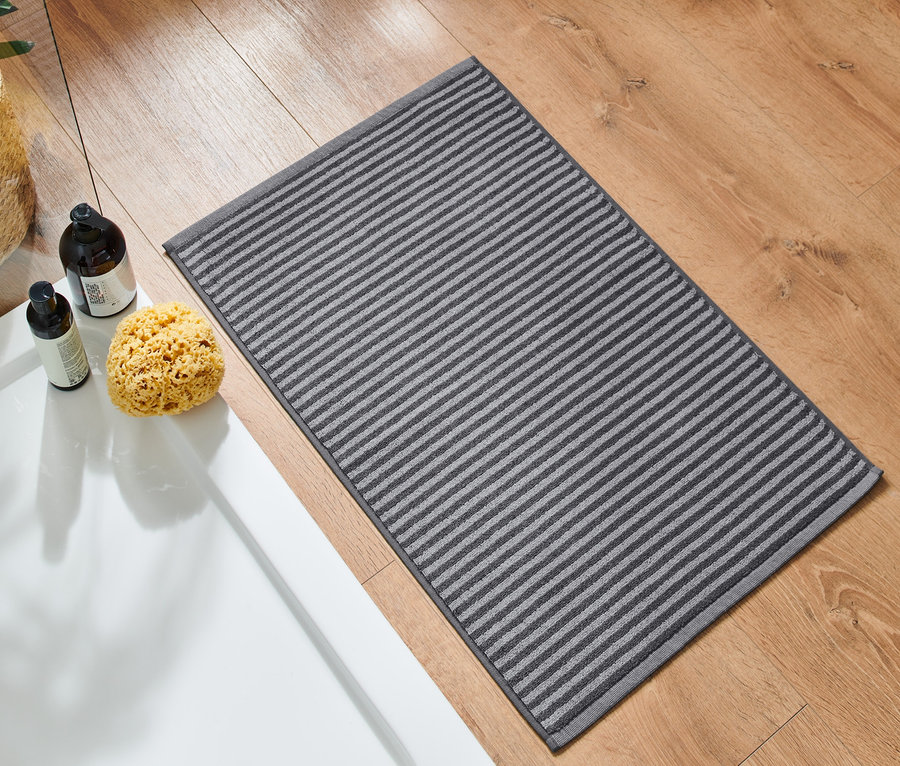 Antrasit renginde kaliteli bir duş paspası, ahşap bir zeminde duşakabinin yanında duruyor.