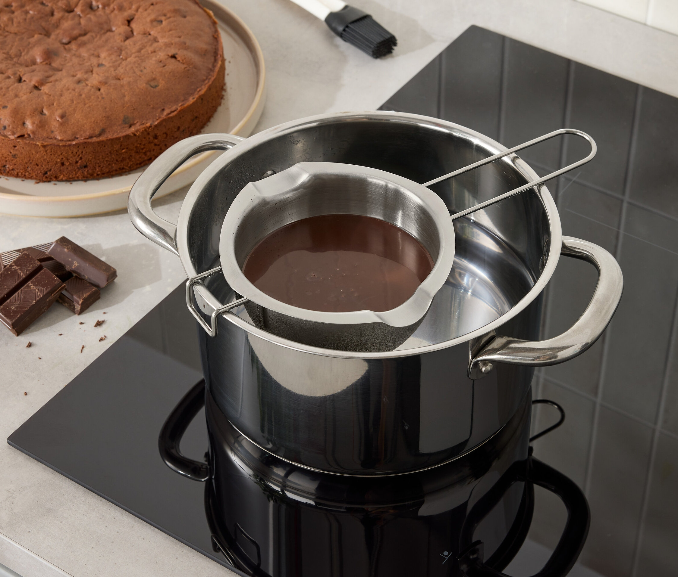 Çikolatalı kek ve çikolata, su dolu bir tencerenin üzerinde paslanmaz çelik bir kapta eriyor.