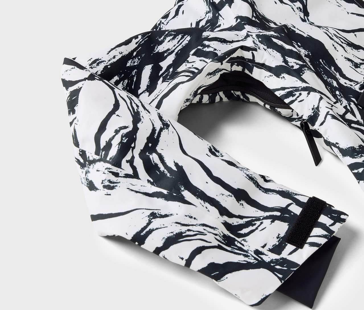 Siyah desenli beyaz bir ceketin, kol ve fermuarı görünen detay çekimi.