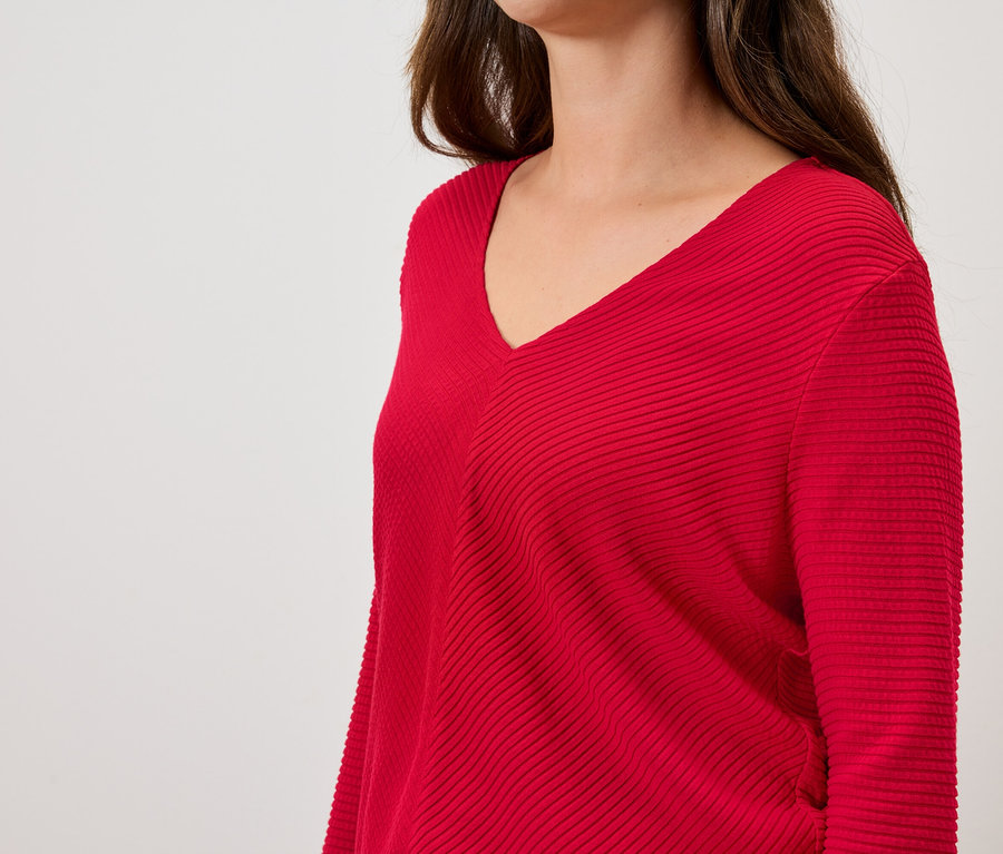 Kadın, uzun kollu ve V yakalı kırmızı bir kazak giyiyor.