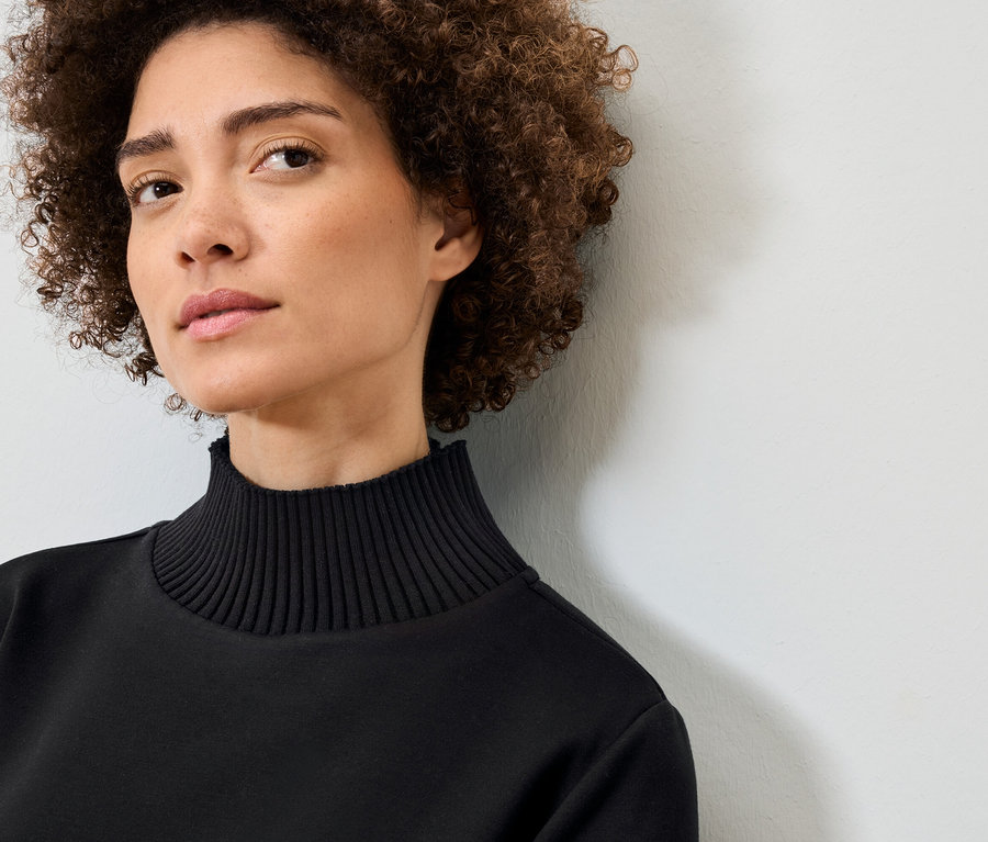 Kıvırcık saçlı, siyah balıkçı yaka kazaklı bir kadının portresi.