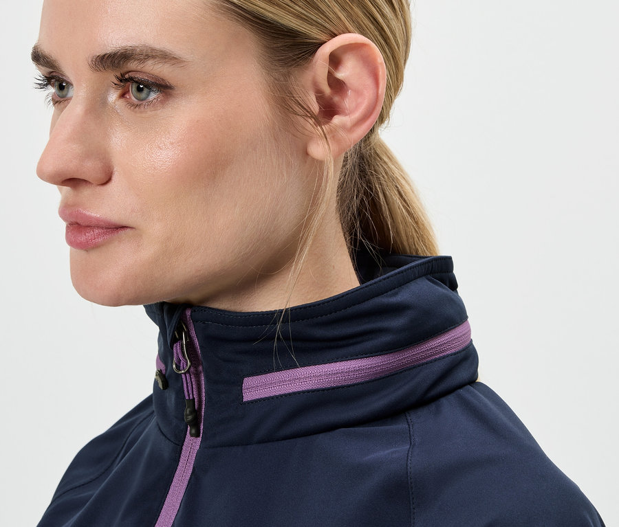 Sarışın saçları at kuyruğu yapılmış, mor detaylı mavi bir ceket giyen bir kadının yüzünün yakın çekimi.