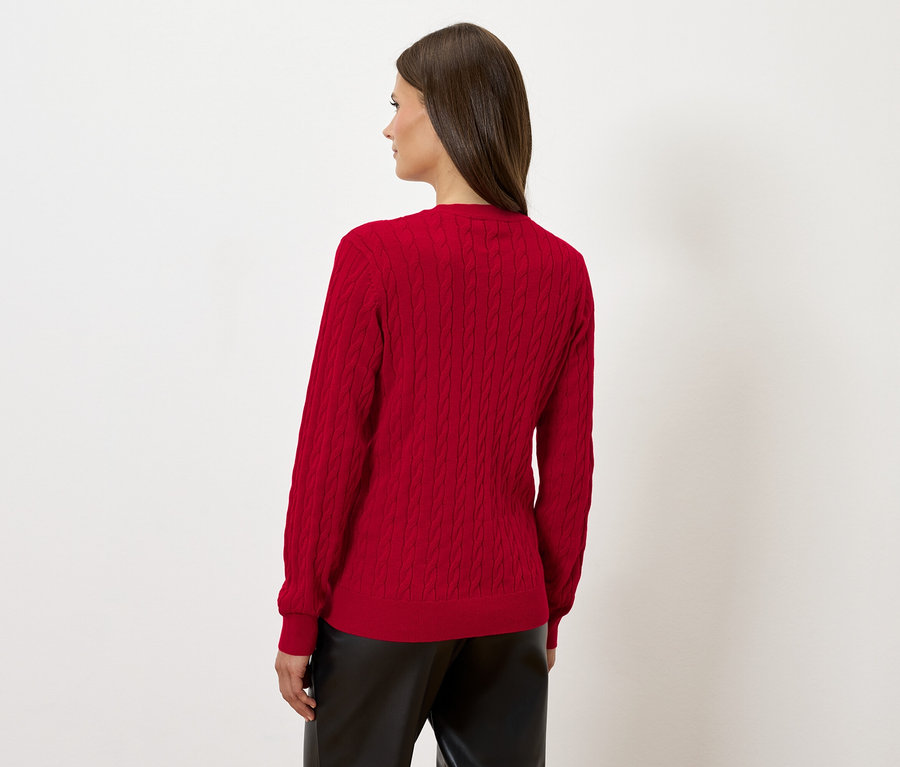 Kadın arkası dönük duruyor, kırmızı bir kazak ve siyah deri pantolon giyiyor.