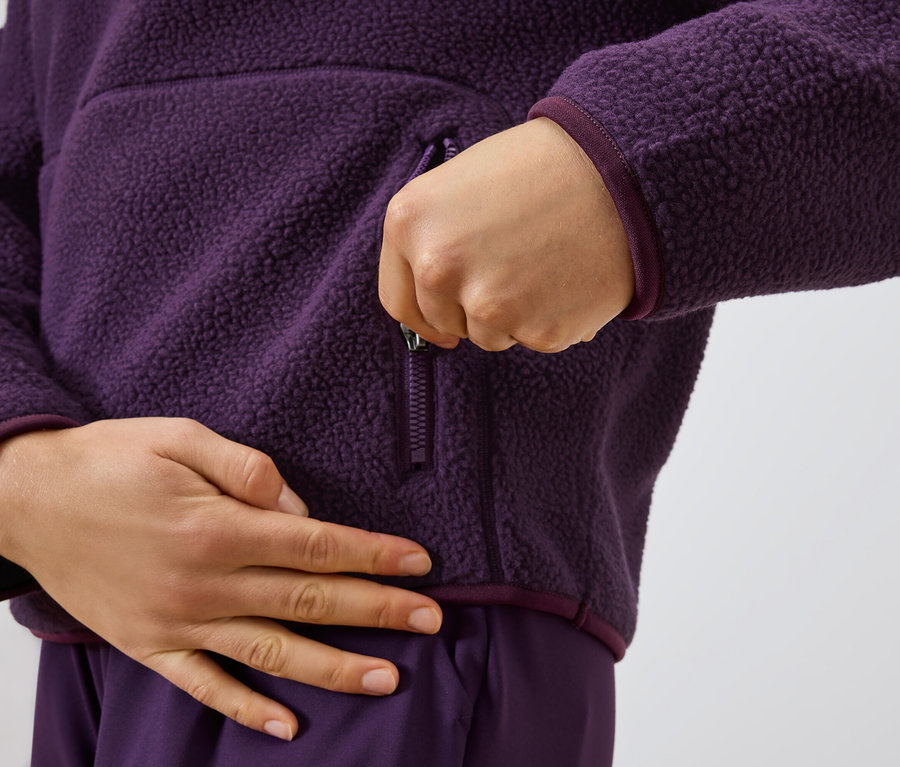 Bir kişi mor renkli bir polar kazağın fermuarını kapatıyor.