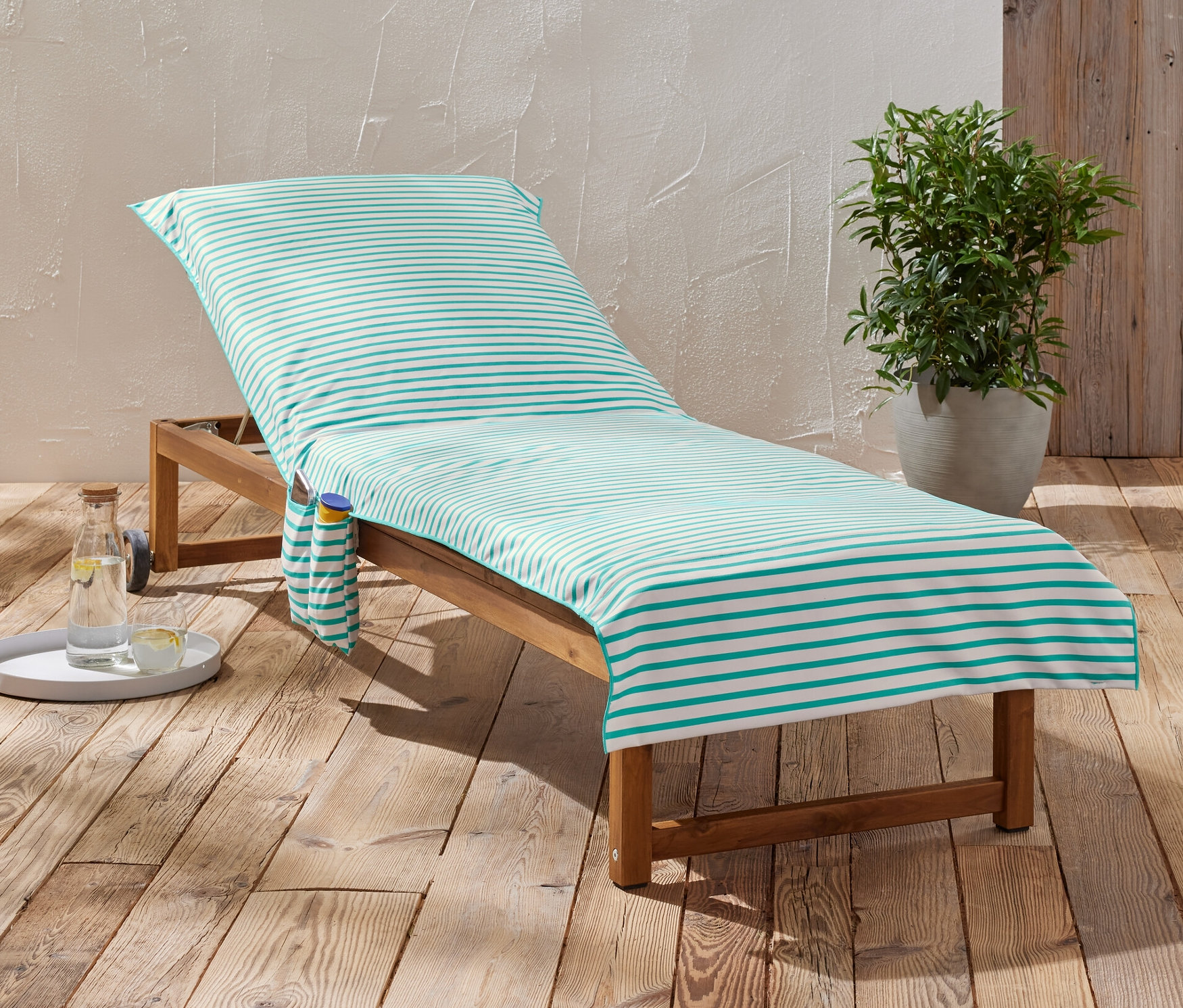 Çizgili bir havlu, bir içecek ve bir bitkinin yanında ahşap bir şezlongda duruyor.