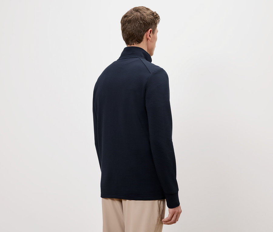 Kahverengi saçlı bir adamın lacivert dik yakalı bir kazak ve bej pantolon giydiği arka görünümü.