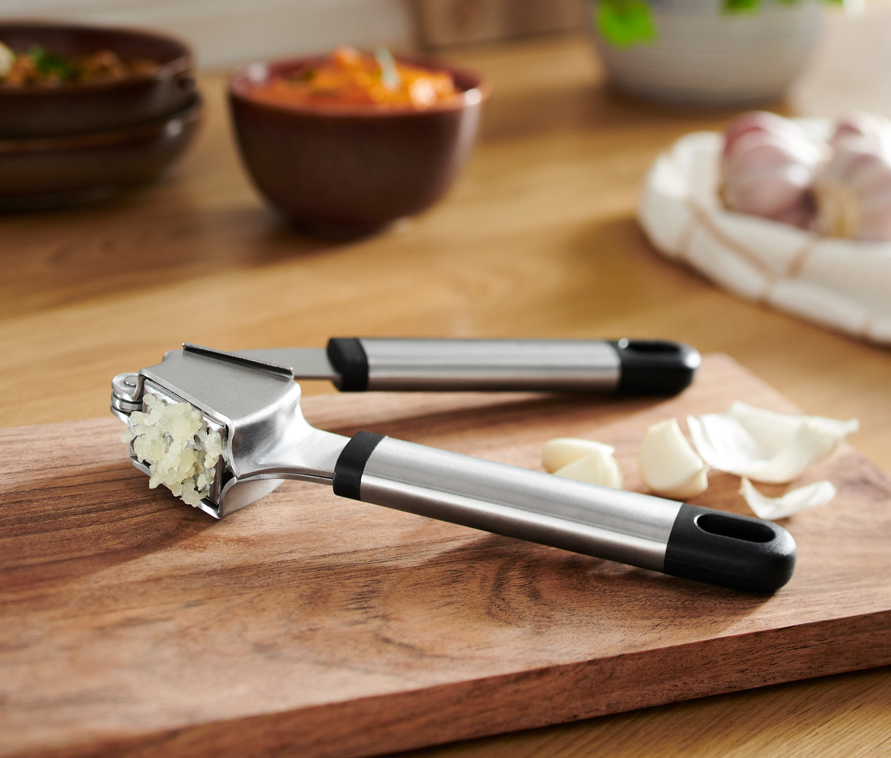 Ahşap kesme tahtası üzerinde ezilmiş sarımsaklı sarımsak ezici.